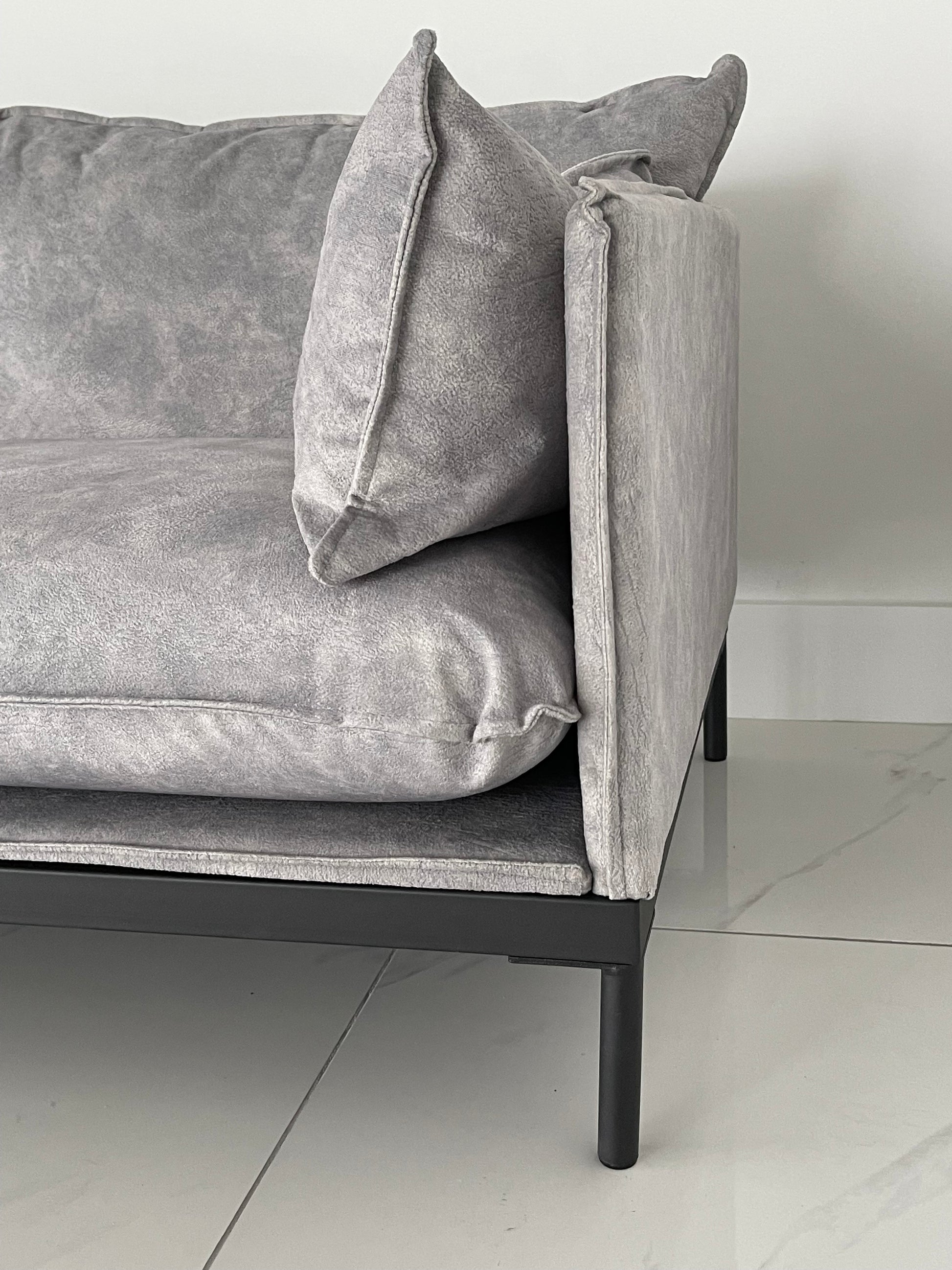 Side view showing thin metal leg frame and plush back cushion on grey office guest seating sofa
