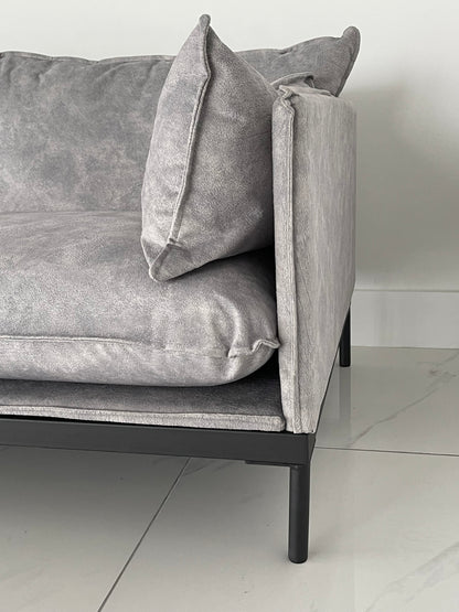 Side view showing thin metal leg frame and plush back cushion on grey office guest seating sofa