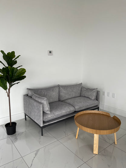 Modern office reception waiting area featuring grey 2-seater couch round wooden table and indoor plant decor